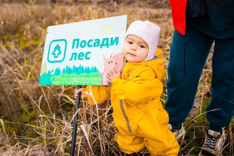 Малыш в жёлтом комбинезоне у таблички «Посади лес»